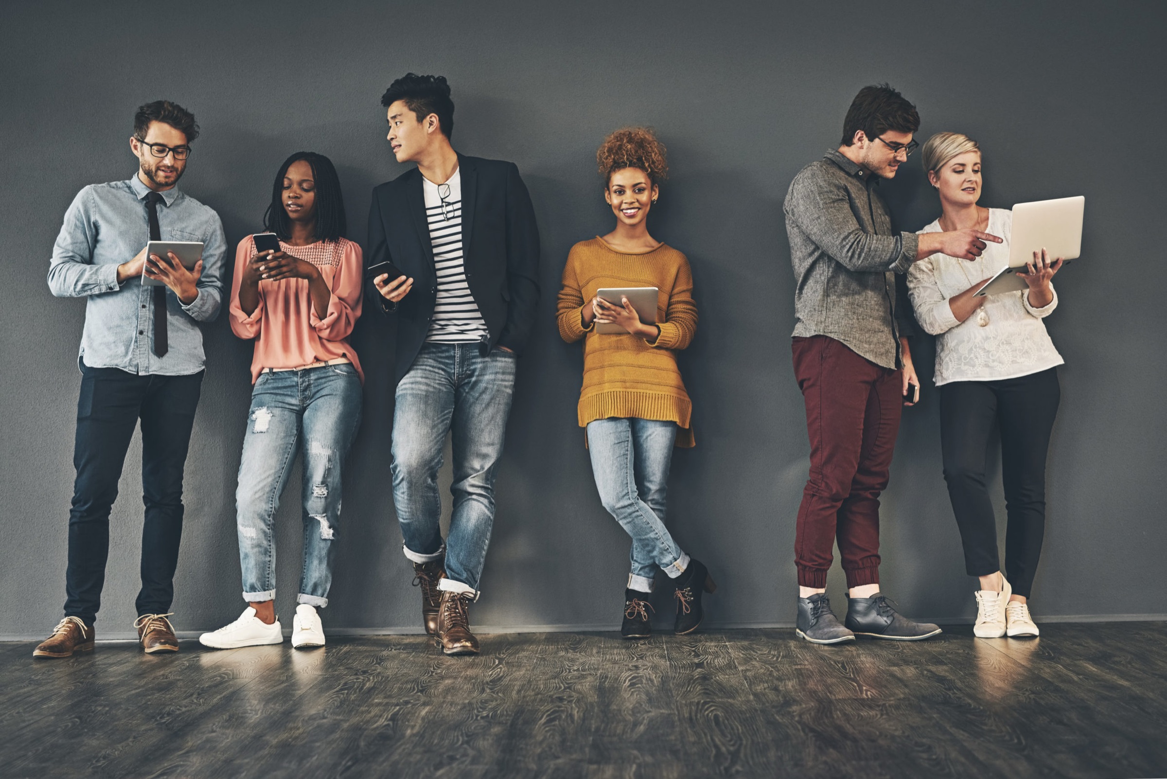 Team mit Smartphones, Tablets und Laptops an einer grauen Wand